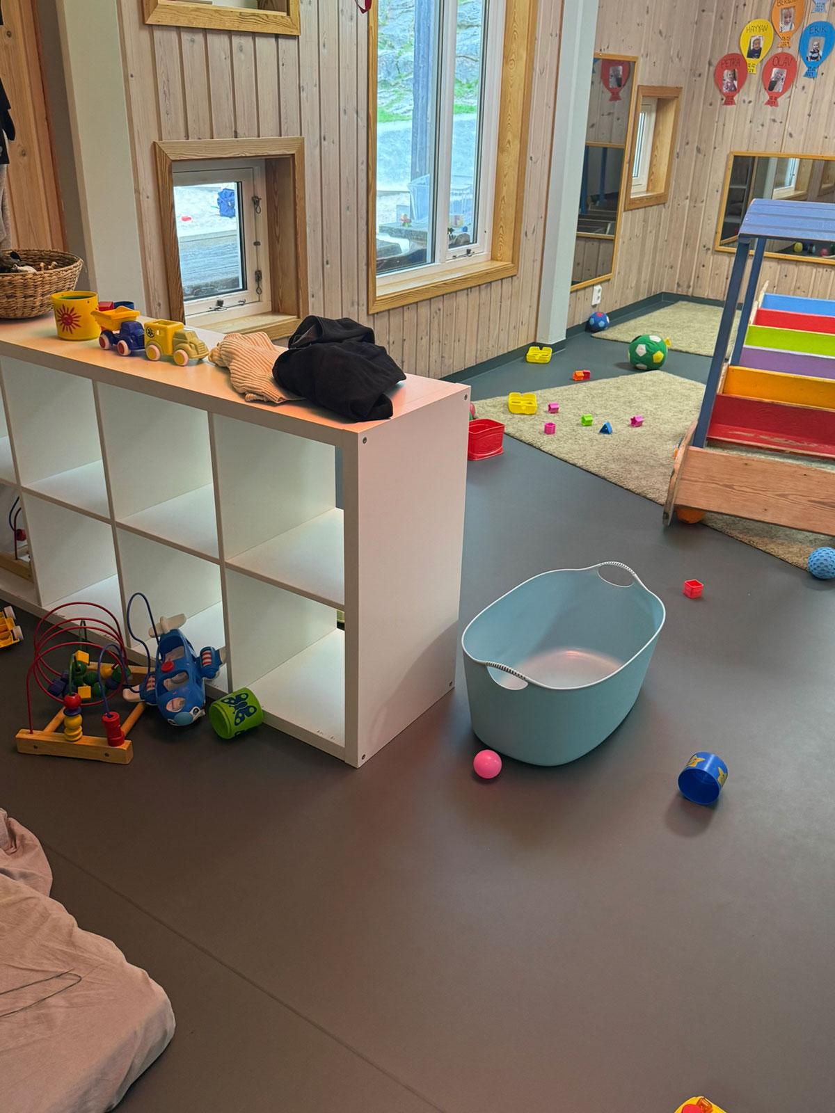 Lekerom i en barnehage med hyller og skap, leker strødd utover gulvet 