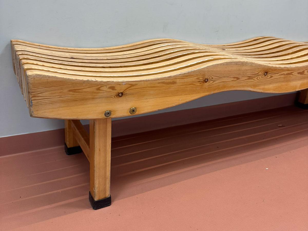 en benk i treverk format sm bølger stående inntil veggen