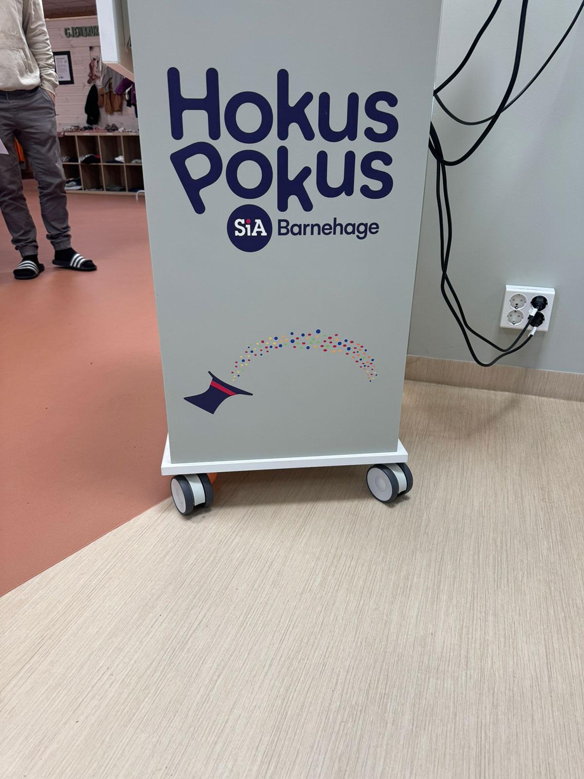 et høyt skap på hjul med påskriften Hokus Pokus Barnehage i blå skrift