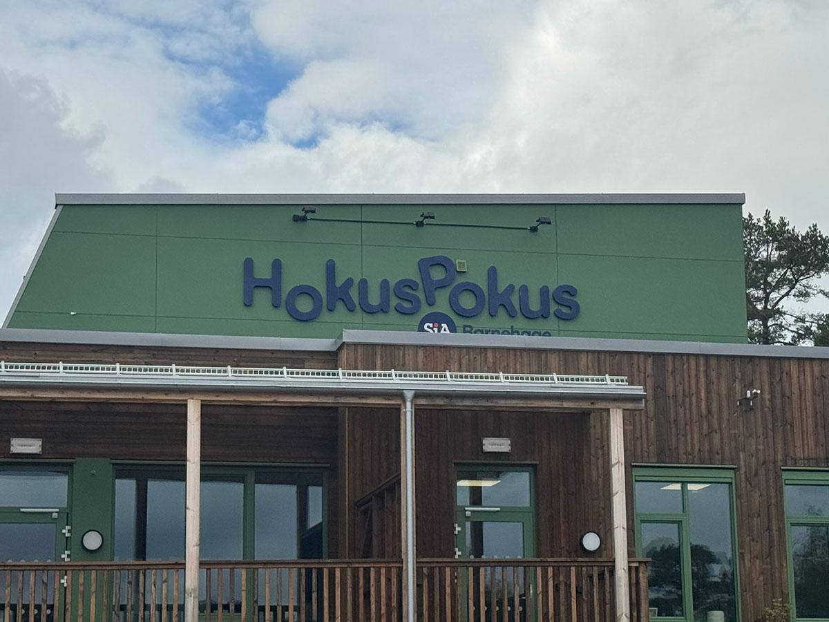 fasaden til Hokus Pokus Barnehage hvor øverste del av bygget er grønt med blå skrift. nederste del er i treverk
