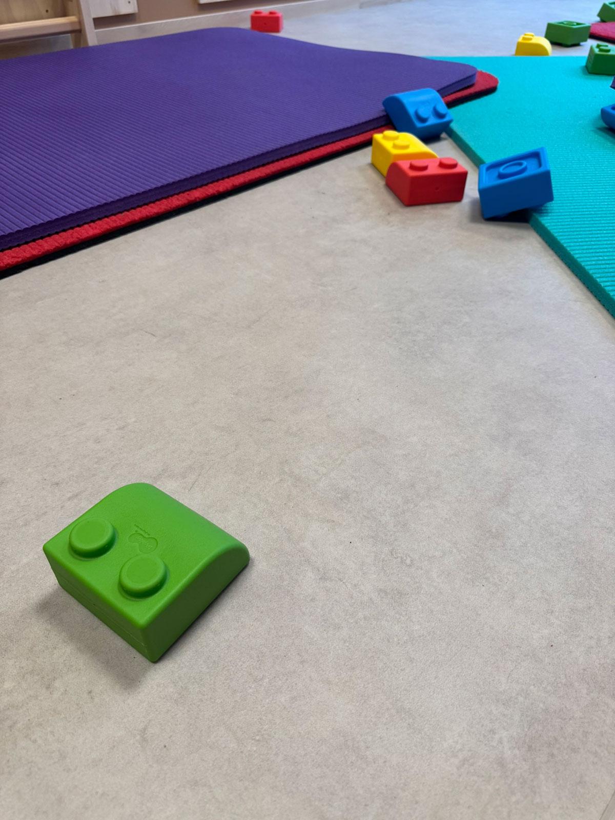 aktivitetsrom i en barnehage med fokus på gulvet. Matter og klosser i sterke farger ligger øverst i bilder. En stor grønn lekekloss i front