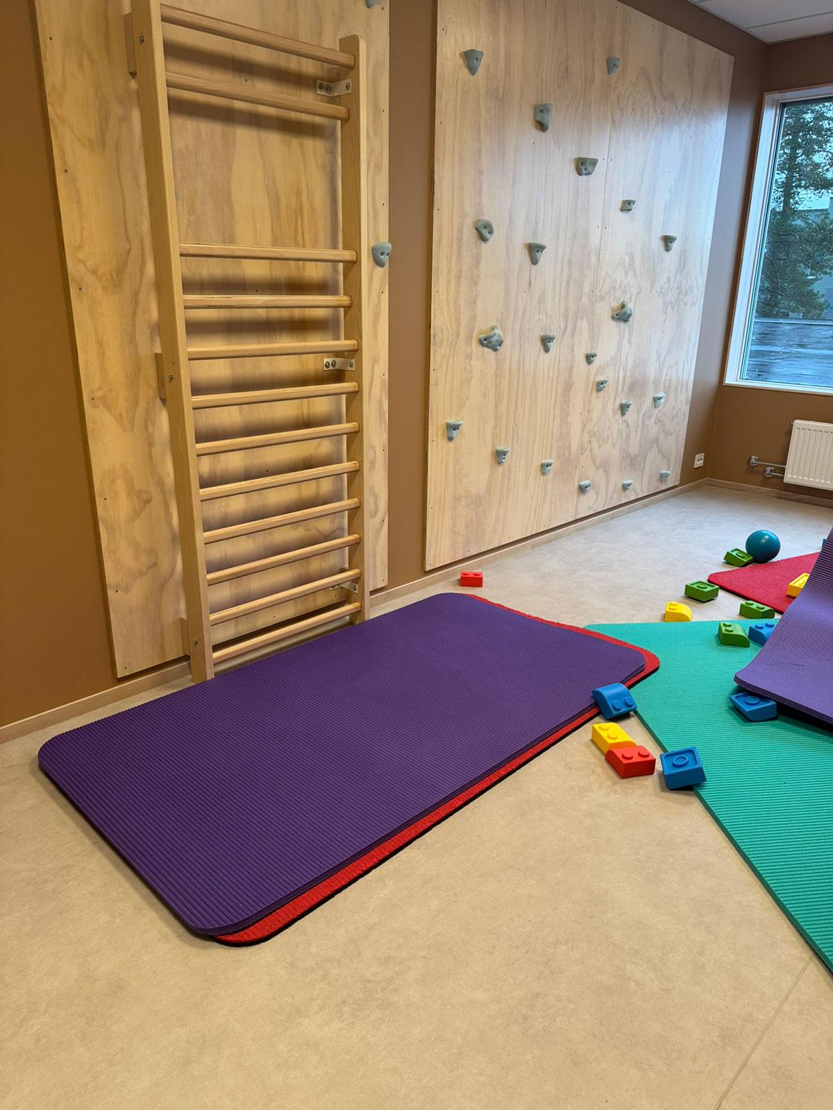 aktivitetsrom i en barnehage med ribbevegg til venstre. matter og lekeklosser i mange ulike sterke farger liggende utover gulvet