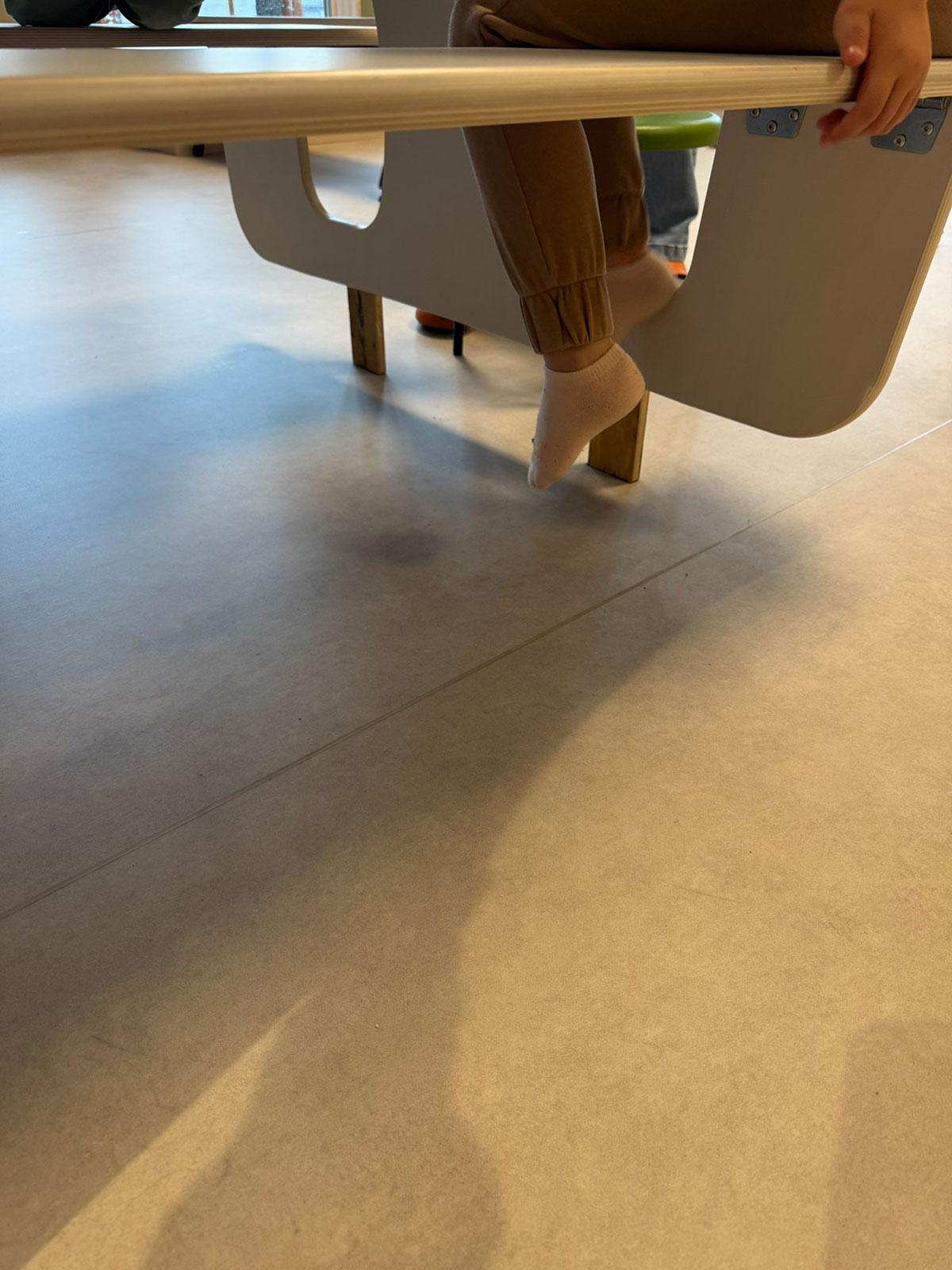 undersiden av en sittebenk med et barn sittende på benken hvor du kun ser nederste del av benene til barnet