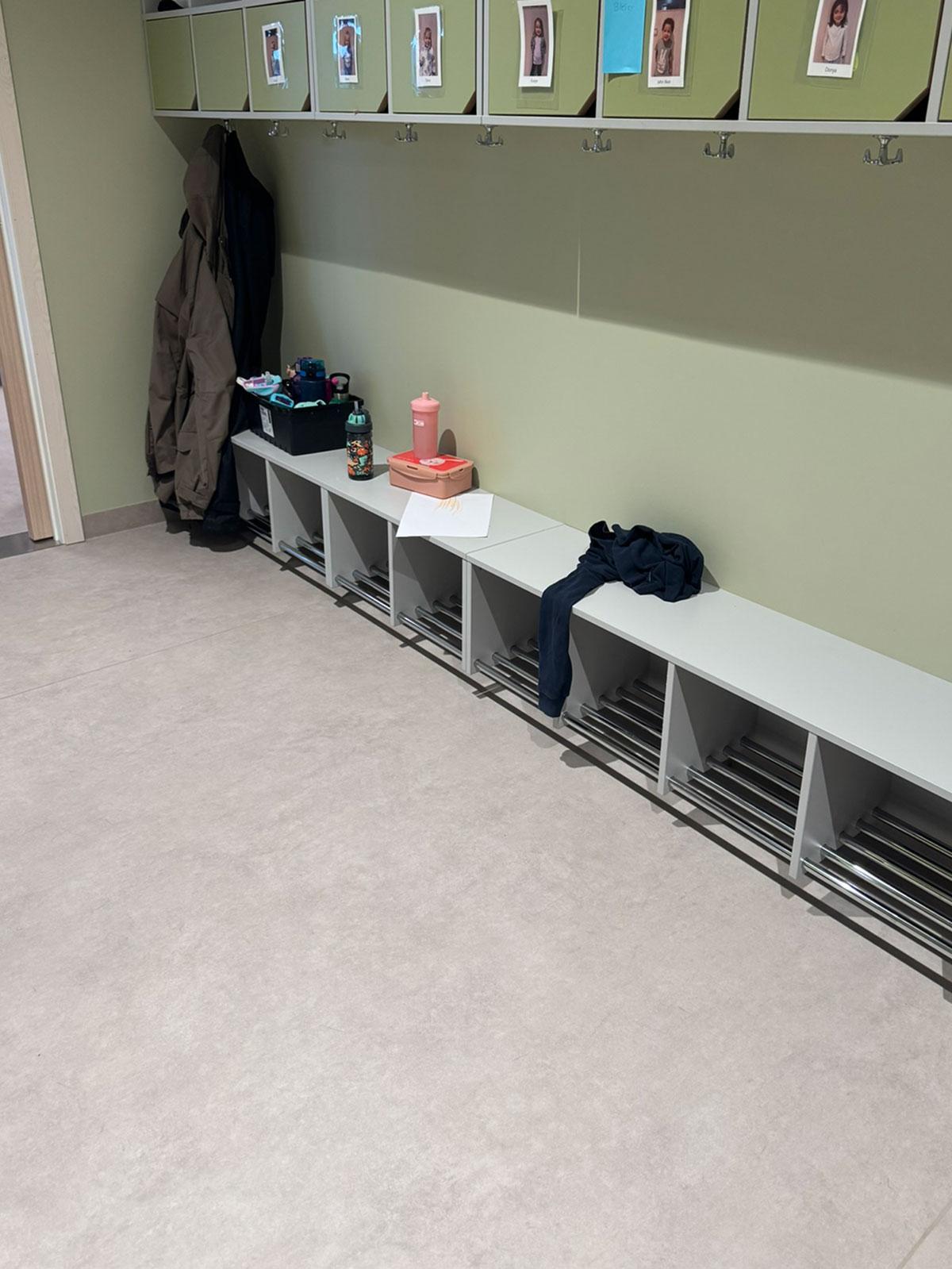 lav benk i gangen eller skifterommet på en barnehage. grønn vegg med skap hengene høyt