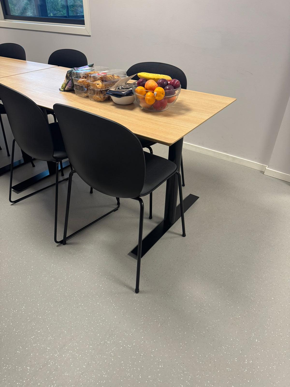 spiserom med langt bord og sorte stoler. En bolle med frukt står på bordet
