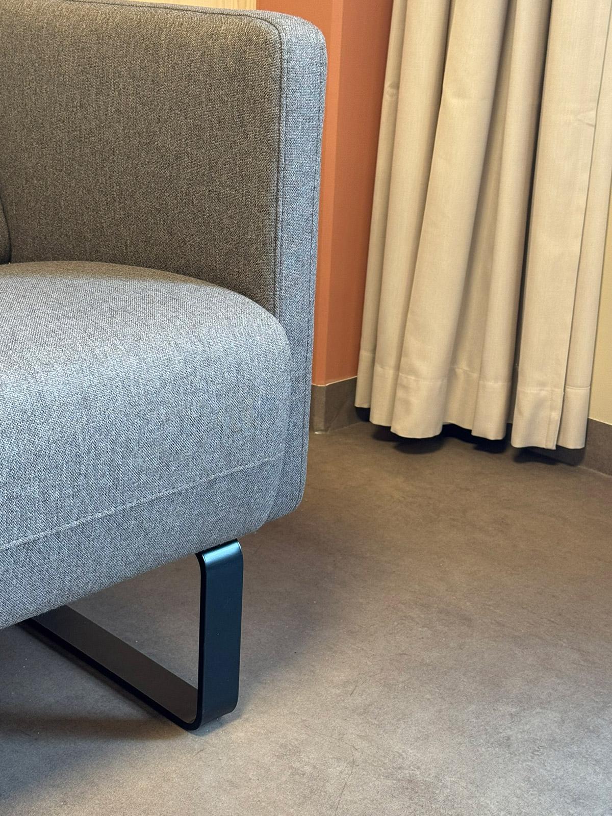 Detaljbilde av moderne grå sofa mot oransje vegg og lyse gardiner i Lund Torv studentboliger.