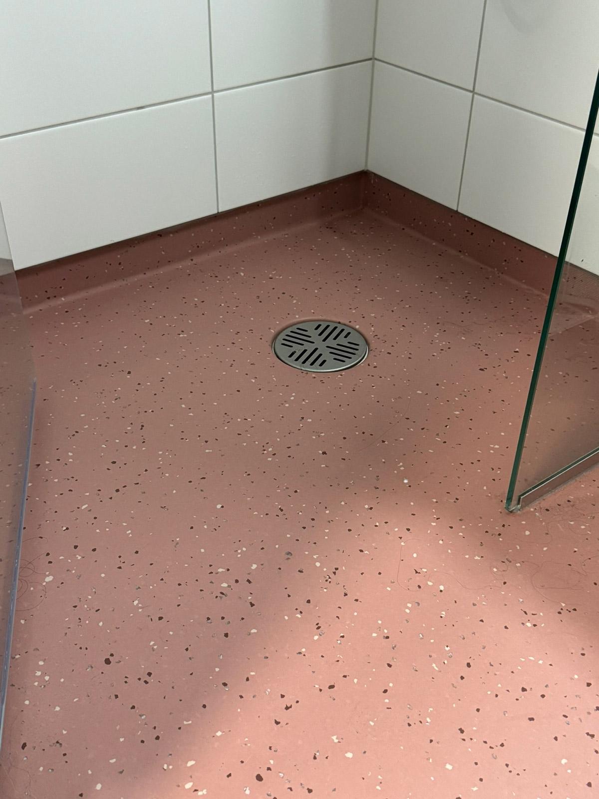 Dusjhjørne med rosa gulvbelegg og hvite fliser i bad på Lund Torv studentboliger.