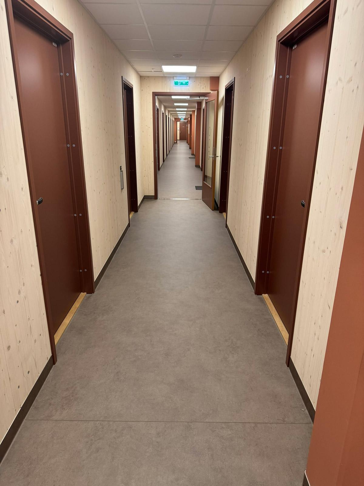 Lang korridor med trepanel og brune dører i Lund Torv studentboliger.