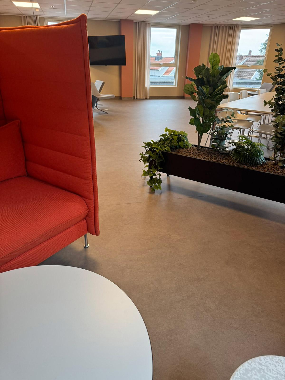 Fellesområde med røde møbler, grønne planter og store vinduer i Lund Torv studentboliger.