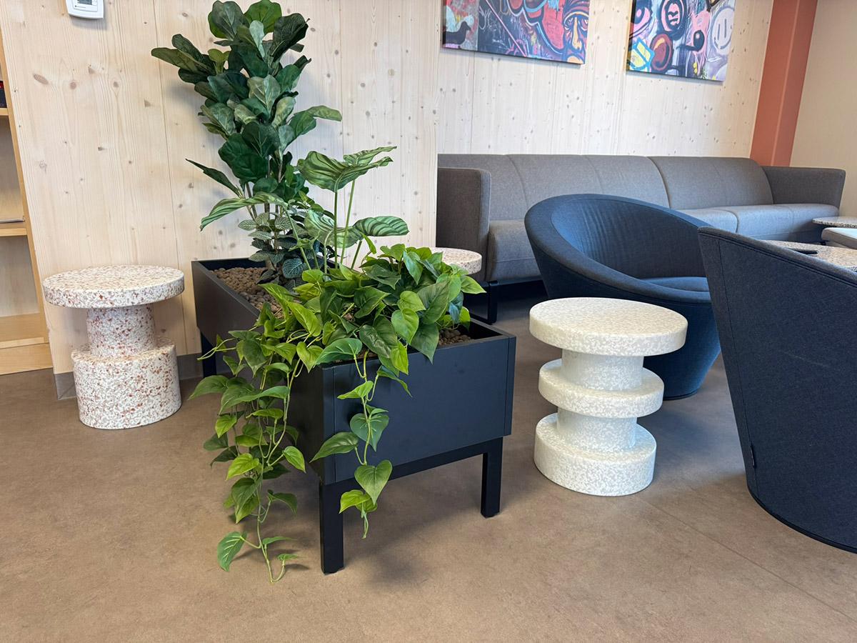 Loungeområde med grønne planter, terrazzo-bord og moderne sittemøbler i Lund Torv studentboliger.