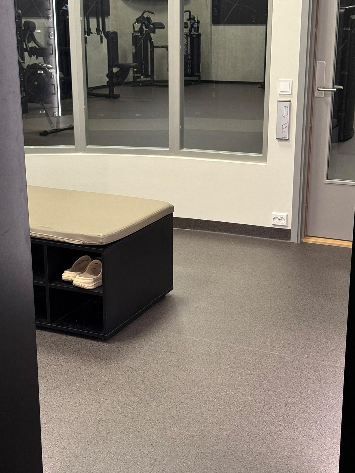Område ved garderobe og treningssal på Spicheren treningssenter, med slitesterkt gulvbelegg og treningsutstyr i bakgrunnen.