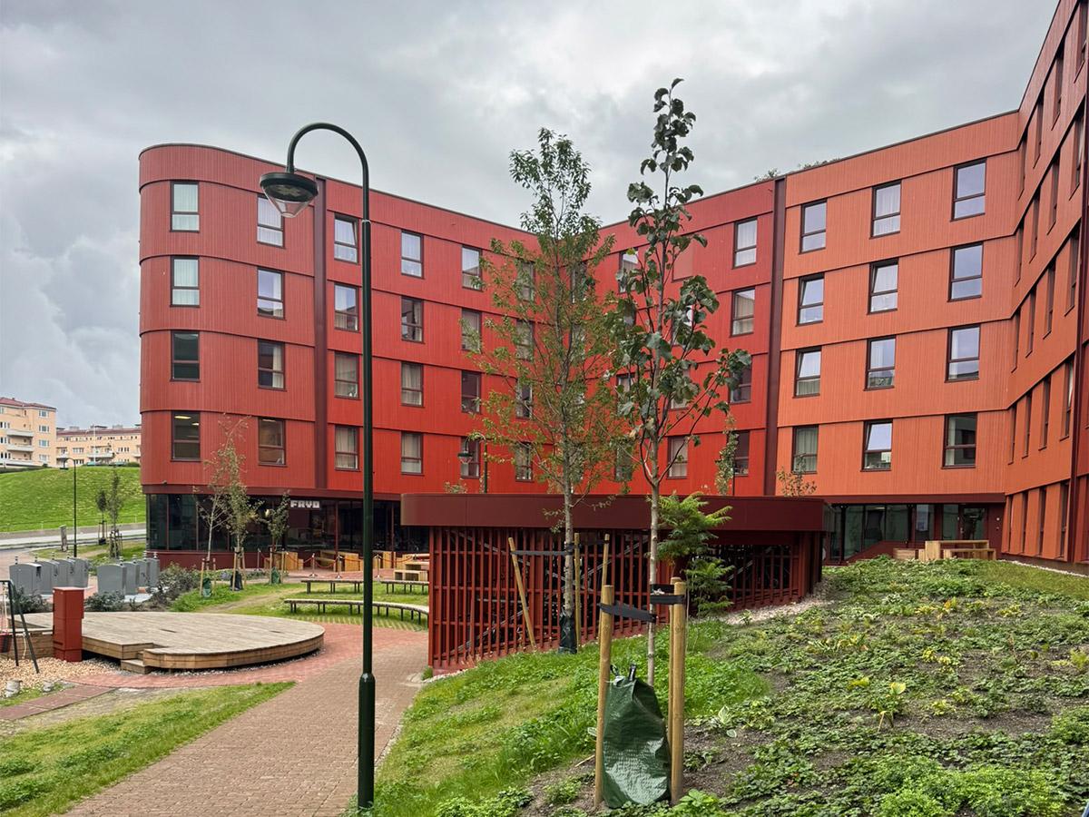 Fasade av Lund Torv studentboliger i Kristiansand med røde paneler og grønt uteområde.
