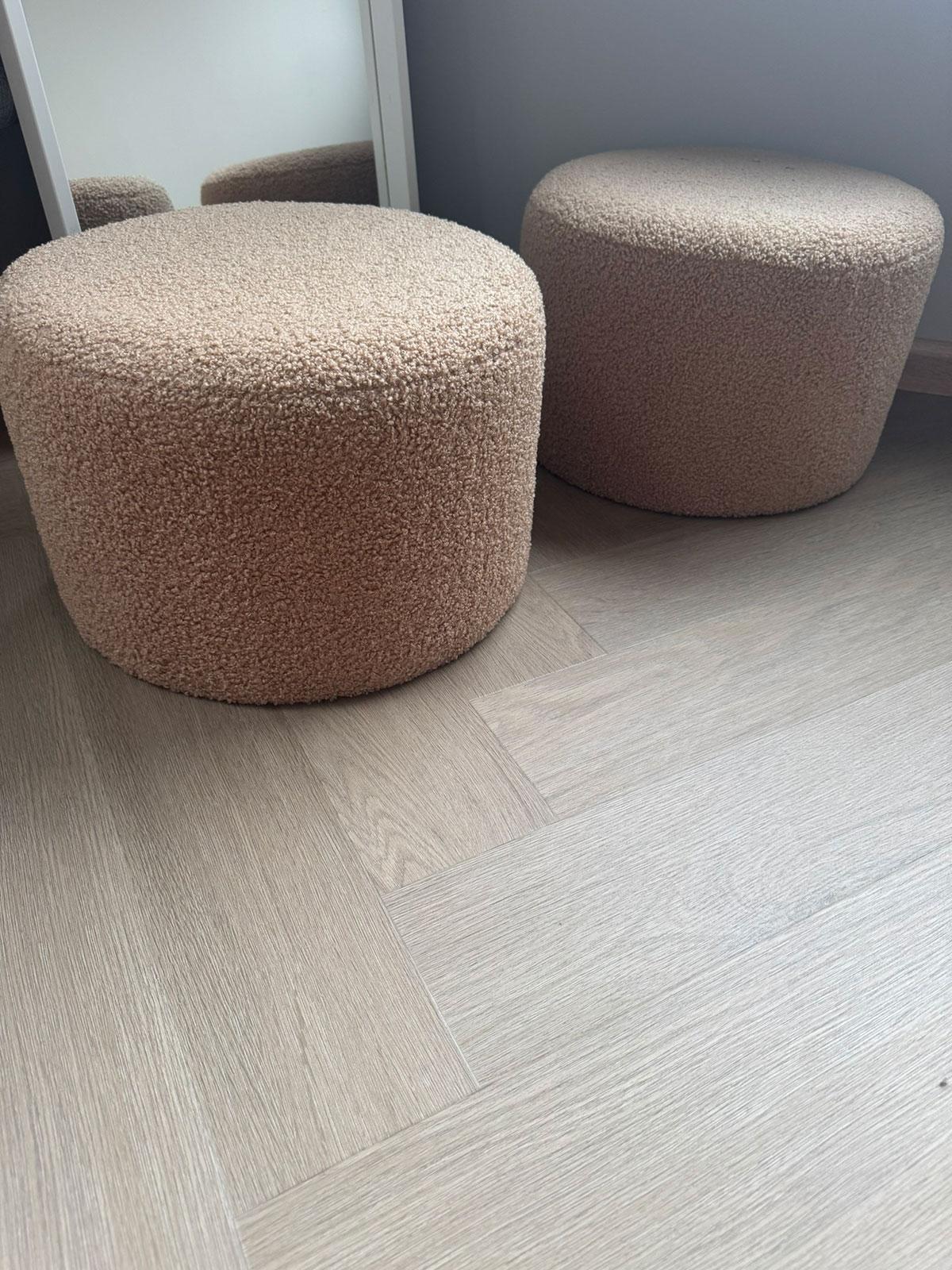 Lys eikefarget LVT-gulv i fiskebensmønster, vist i et moderne interiør med to beige puff-stoler.