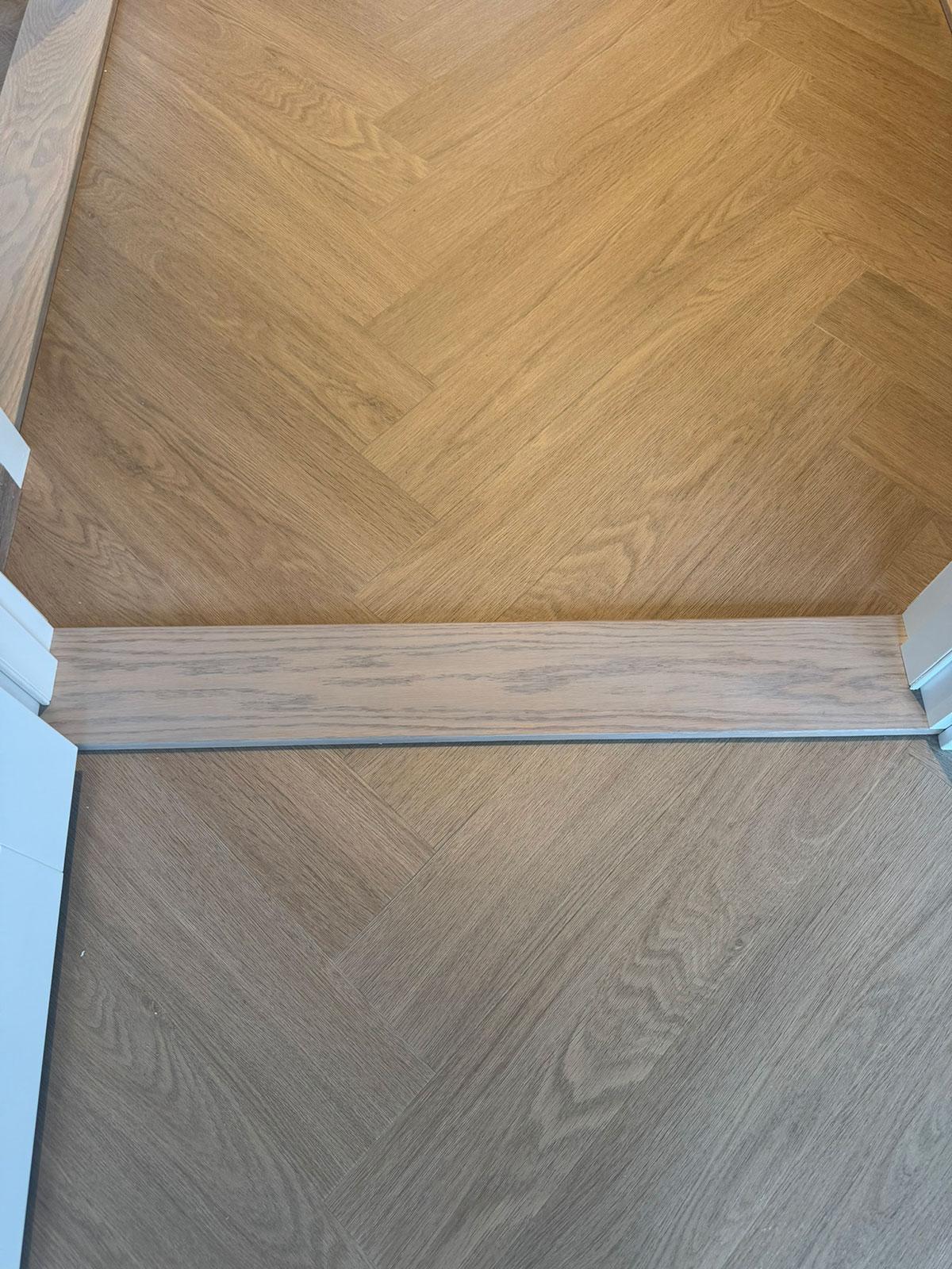 To rom med LVT-gulv i fiskebensmønster, adskilt av en elegant overgangslist i samme stil.