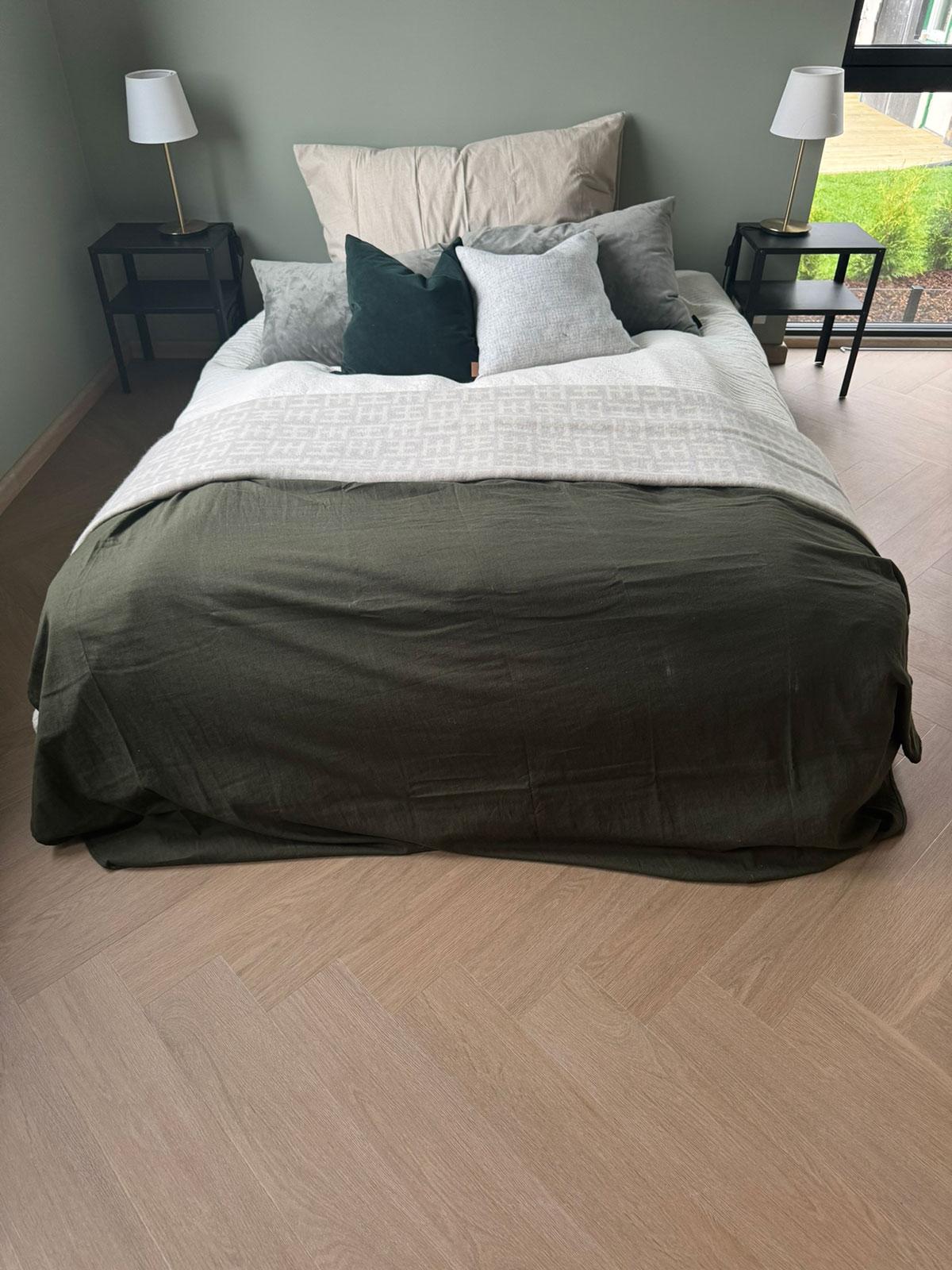 Soverom med lyst LVT-gulv i fiskebensmønster, innredet med grønn sengeteppe, nøytrale tekstiler og moderne nattbordslamper som skaper et harmonisk uttrykk.