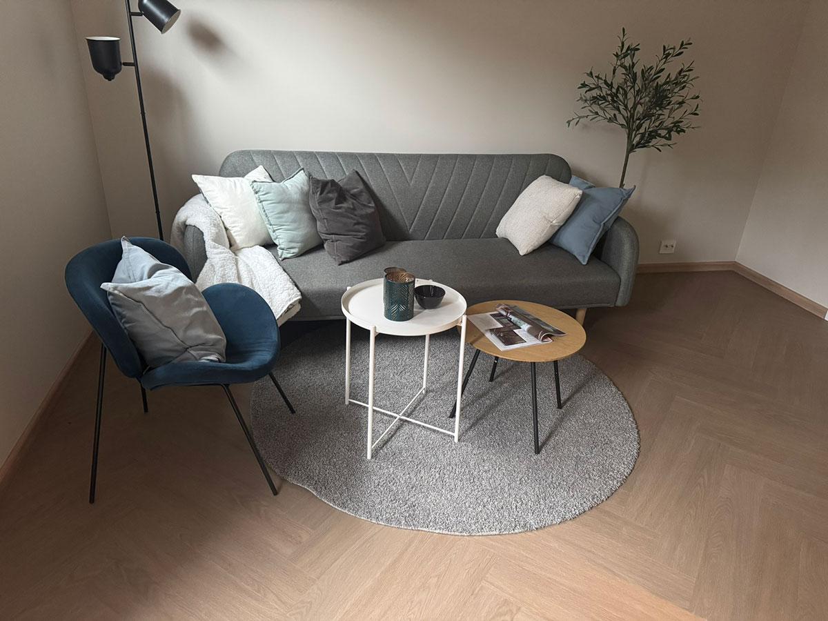 LVT-gulv i lys eikefarge lagt i fiskebensmønster, vist i en moderne stue med sofa, lenestol og runde bord i myke nøytrale toner.