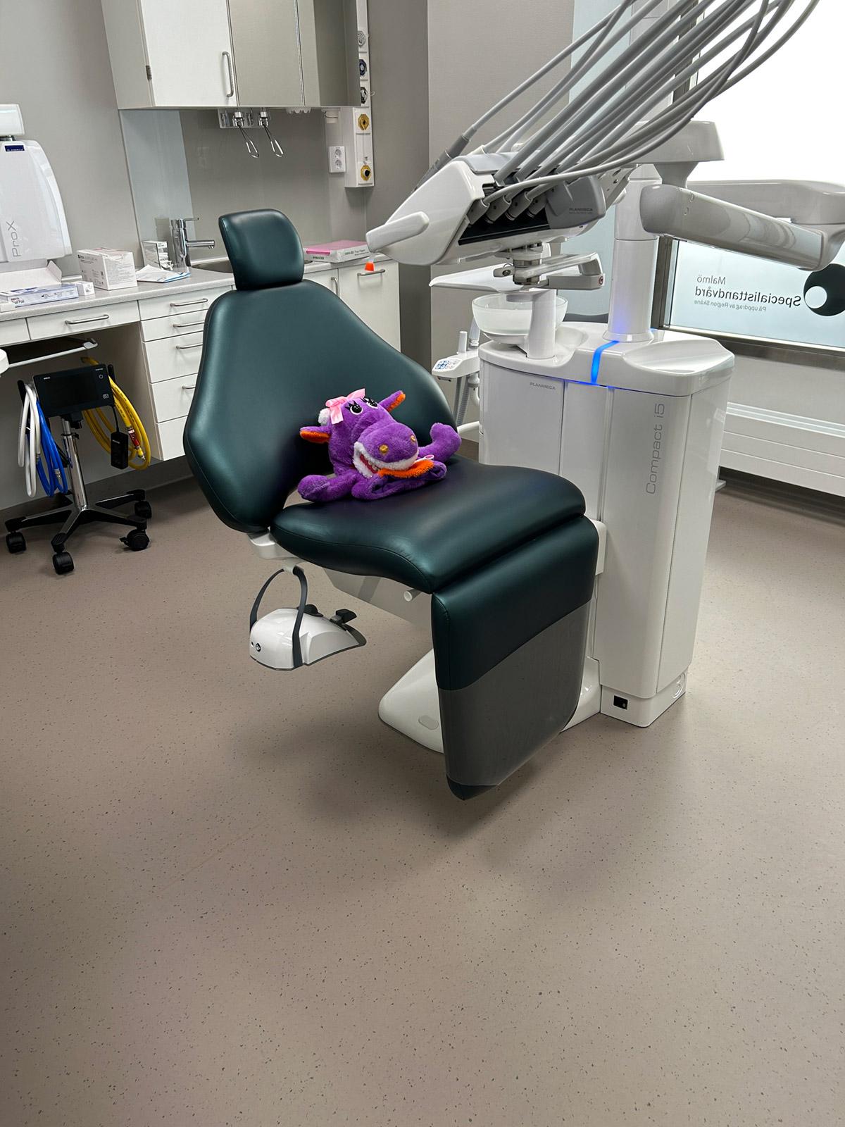 Tannlegebehandlingsrom med grønn behandlingsstol, teknisk utstyr og lyst, slitesterkt gulv med diskret prikkmønster.