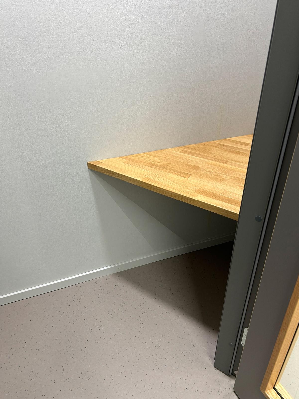 Lite rom med veggmontert trebenk, lyse vegger og lyst gulv med diskret prikkmønster.